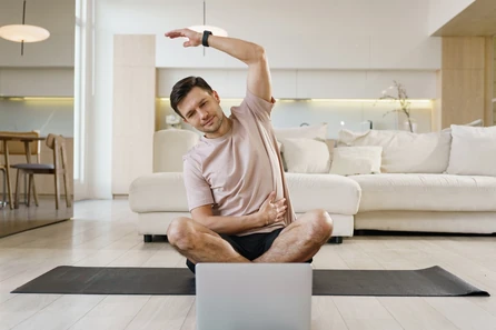 Man stretching at home in front of a laptop